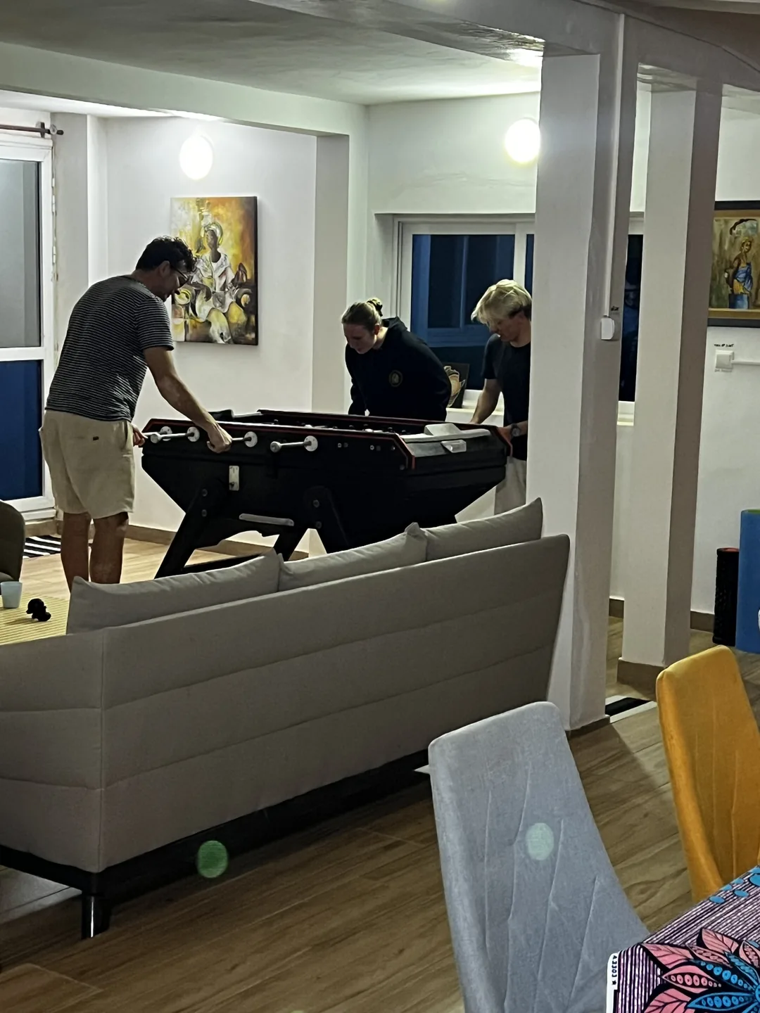 Trois personnes s'amusent autour d'une table de baby-foot dans un surfcamp au Sénégal.