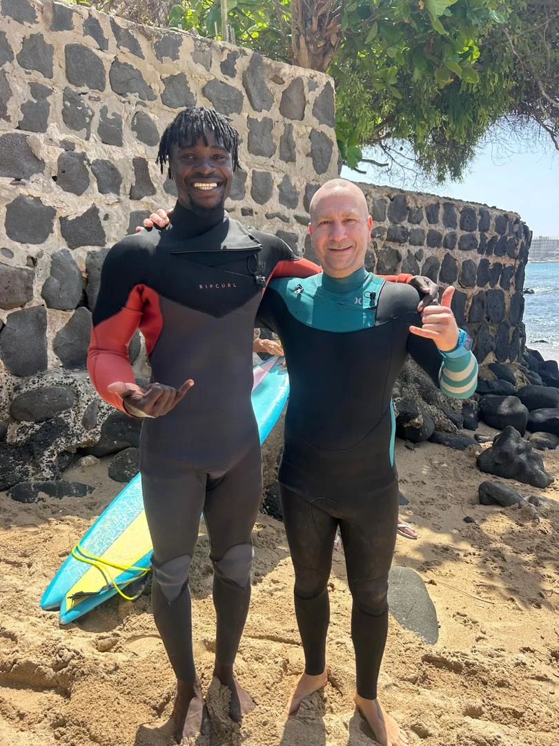 Deux surfeurs souriants posent sur la plage de l'île de Ngor au Sénégal.