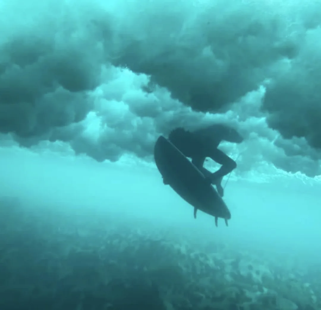 Un surfeur plonge sous une vague au Sénégal, capturant l'énergie de l'océan.