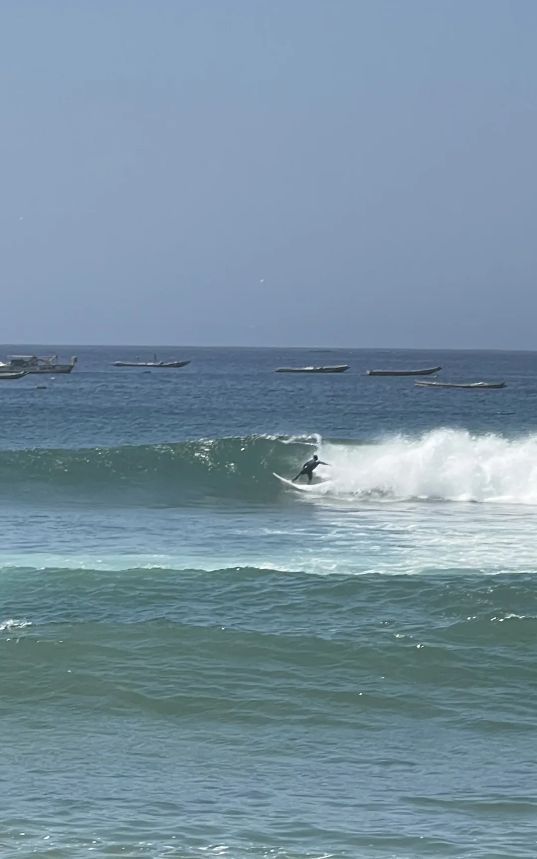 Un surfeur glisse sur les vagues à Ngor, Sénégal, sous un ciel ensoleillé.
